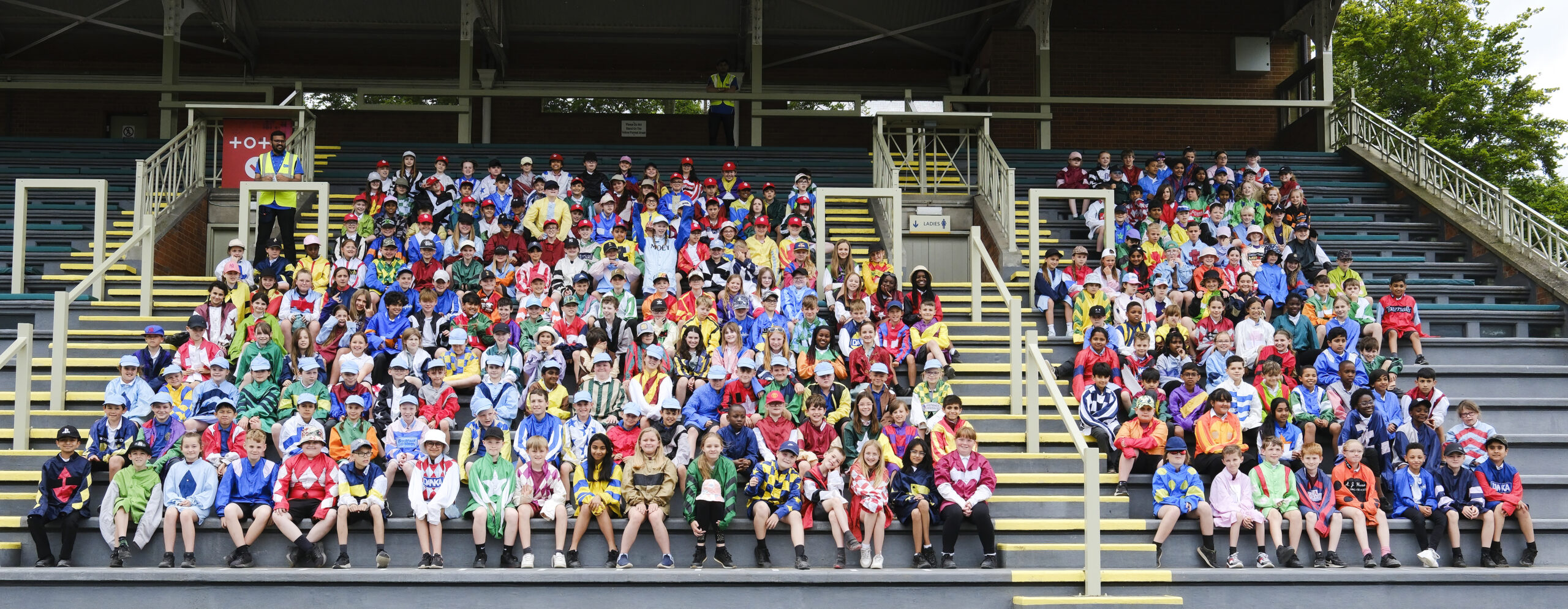 Over 300 year 5 students in colourful racing silks pose for a photograph on the stands.